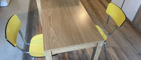 A wooden dining table with four chairs, a magazine rack, and a white cabinet in the background.