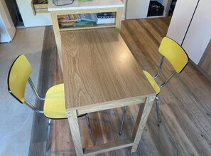 Ein Holztisch mit vier Stühlen, einem Zeitschriftenständer und einer weißen Kommode im Hintergrund.