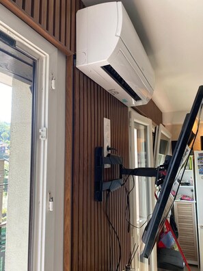 Ein Zimmer mit einer Schiebetür, einer an der Wand montierten Klimaanlage und einem Fenster mit Blick ins Freie.