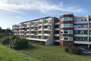 A multi-story residential building with balconies, a flat roof, and a parking area in front. - 38 in the villa by the sea (Grömitz)