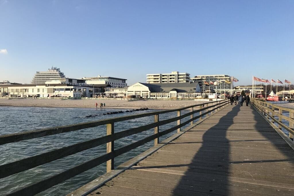 Een houten looppad dat naar een strand leidt, met gebouwen op de achtergrond.