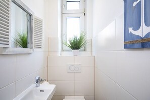 A bathroom with a white sink, a window with shutters, a potted plant, and a towel rack. - Holiday apartment with 1 bedroom (Travemünde)