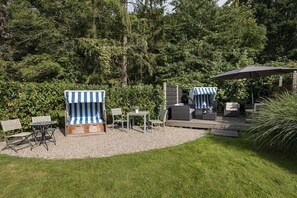A patio area with outdoor furniture, including chairs and tables, surrounded by a gravel area and greenery. - Holiday apartment with 1 bedroom (Travemünde)