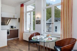 A modern kitchen with a dining area, large windows, and a view of a house. - Villa Agnes Apartment 11 (Binz)