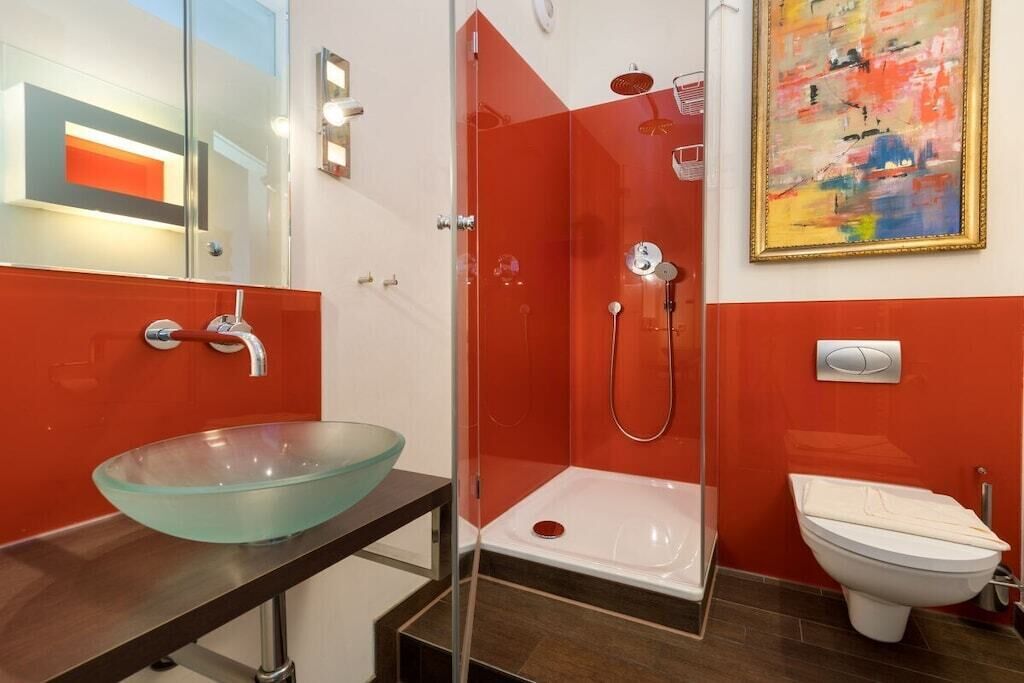 Un bagno moderno con un lavandino a forma di coppa in vetro, una doccia a filo pavimento e un water.