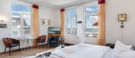 Habitación de hotel con una cama grande, un escritorio con silla, televisión y vista al mar.