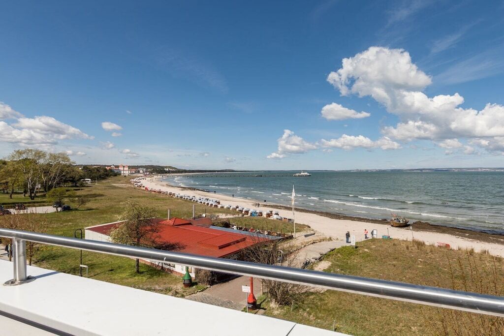 A coastal view with a beach, a red-roofed building, and a clear sky.