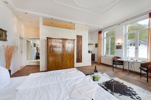 Hotellihuone, jossa on suuri sänky, puinen vaatekaappi, ruokailutila pöytineen ja tuoleineen sekä näkymä ulos.