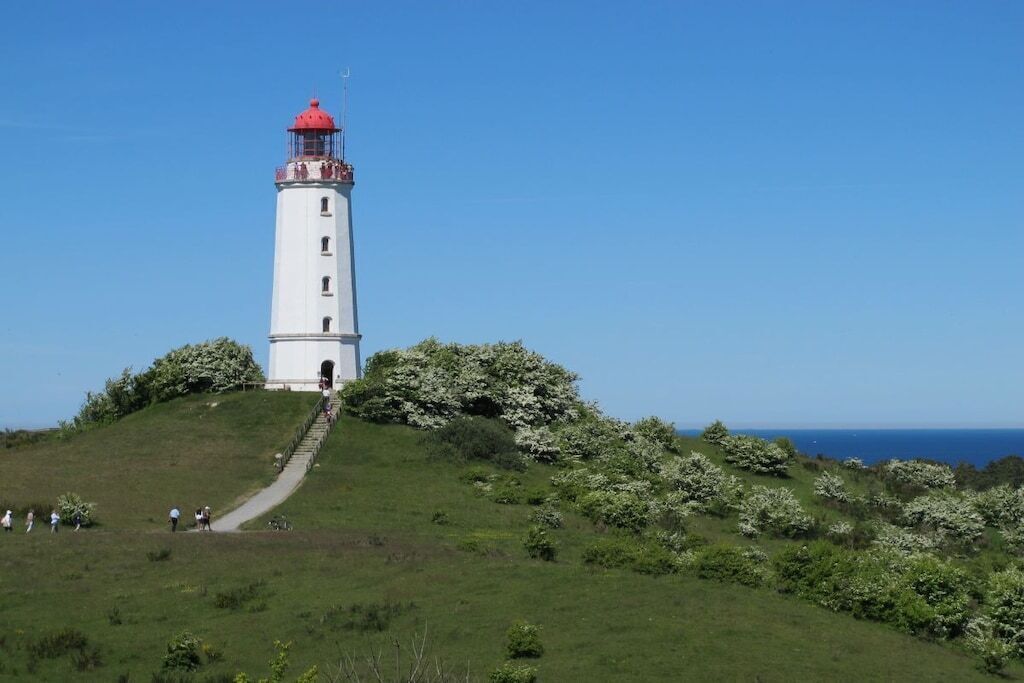 Um farol numa colina gramada, com vista ampla para o oceano.