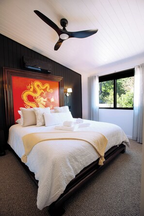 Ett hotellrum med en stor säng, en takfläkt, en tavla med en röd drake och ett fönster med utsikt över grönområden.