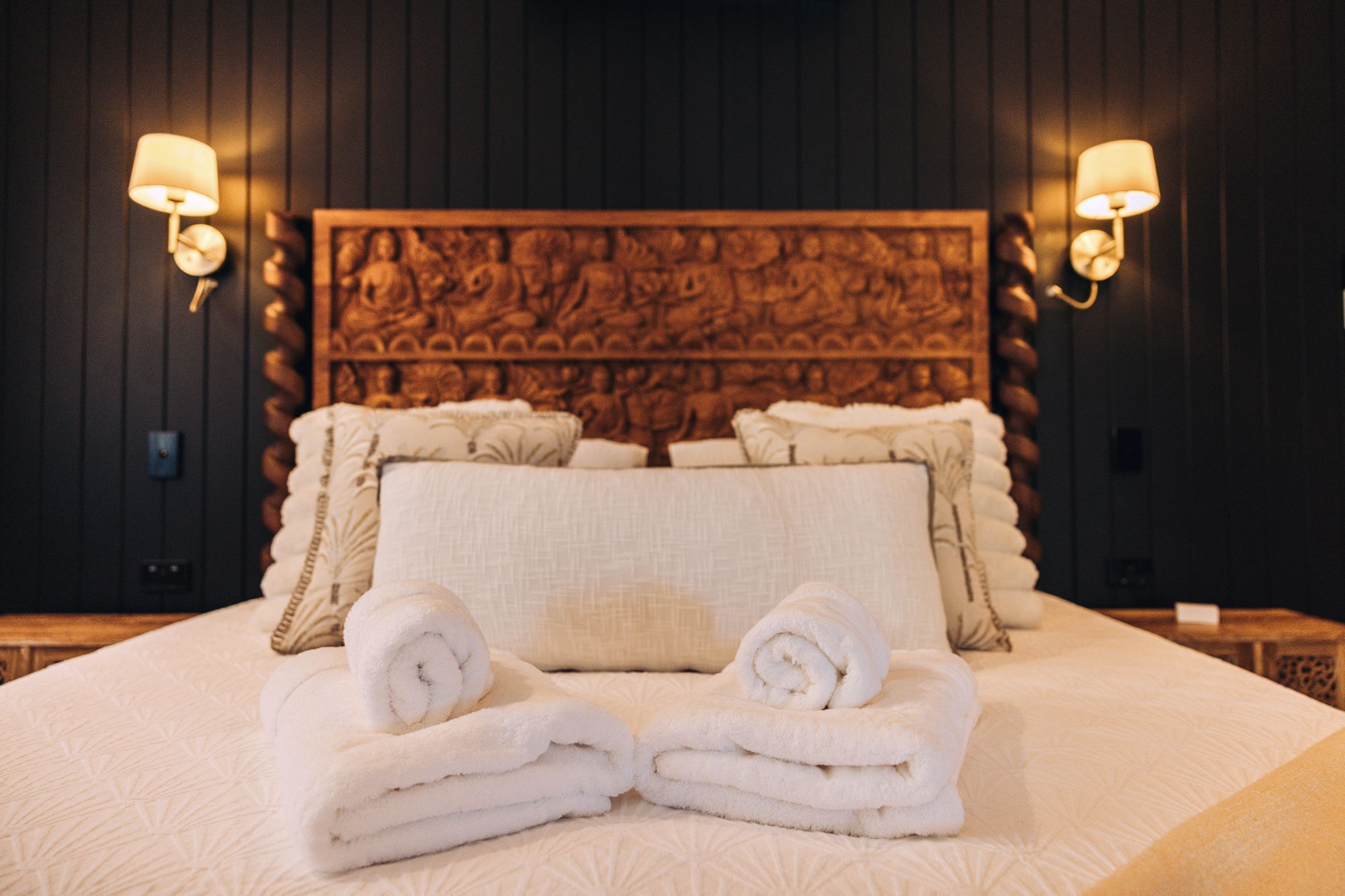 A hotel room with a large bed, two wall-mounted lamps, and a decorative headboard.