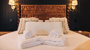 Quarto de hotel com uma cama grande, duas luminárias na parede e uma cabeceira decorativa.