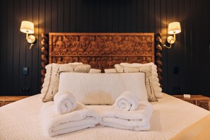 Ett hotellrum med en stor säng, två väggmonterade lampor och en dekorativ sänggavel.