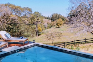 Une piscine dotée d’une terrasse en bois et de chaises longues, entourée d’une clôture et d’arbres.