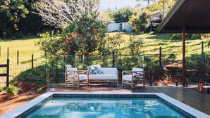 Piscina com deck de madeira, rodeada por um quintal cercado com árvores e um edifício ao fundo.