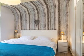 Ein Schlafzimmer mit einem Bett, zwei Nachttischen mit Lampen, einer Holzwand mit einer herzförmigen Dekoration und einer blauen Tagesdecke.