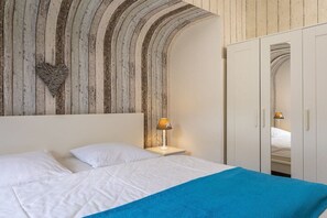 Ein Schlafzimmer mit einem Bett, weißen Kissen, einer blauen Decke, einer Wanddekoration in Herzform und einem Kleiderschrank mit Spiegel.