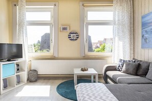 Ein modernes Wohnzimmer mit Fernseher, Sofa und Blick auf Gebäude durch große Fenster.