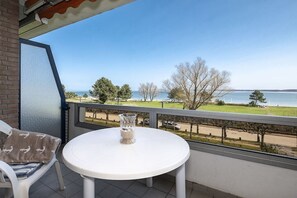 A balcony with a white table and chair, overlooking a body of water and a grassy area. - Holiday apartment with 1 bedroom (Travemünde)