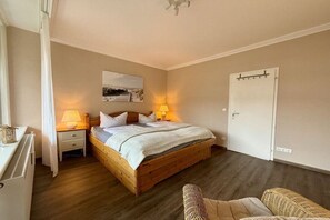 A bedroom with a wooden bed, bedside lamps, a white door, and a small bedside table. - Holiday apartment with 1 bedroom (Travemünde)