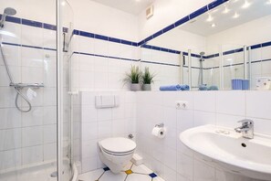 A bathroom with a glass-enclosed shower, a white toilet, a sink with a mirror, and a potted plant. - Holiday apartment with 1 bedroom (Travemünde)