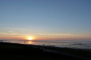 Un coucher de soleil sur une plage, avec un sentier et quelques constructions.