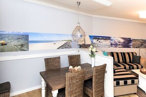 A dining area with wicker furniture and a white table, a sofa with striped cushions, and a hanging light fixture. - Beach Palace Apt. 108 (Cuxhaven)