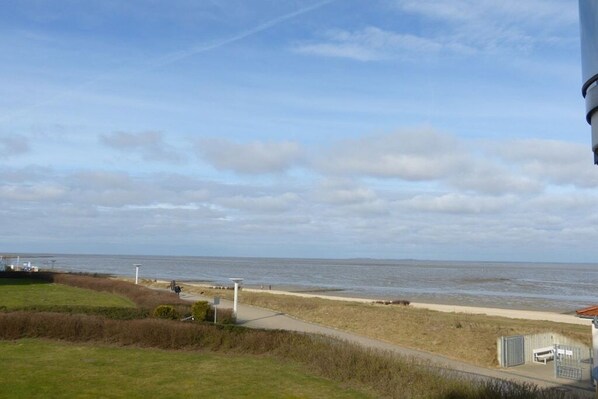 A coastal view with a pathway leading to the beach, a fence, and a building with a red roof. - Beach Palace Apt. 108 (Cuxhaven)