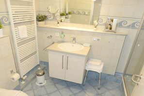 A bathroom with a white sink, a towel rack, a mirror, and a small trash bin. - Beach Palace Apt. 108 (Cuxhaven)