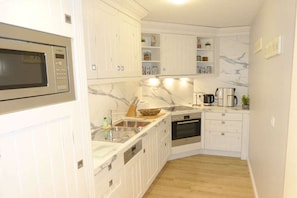 A compact kitchen with white cabinetry, a built-in microwave, a sink, and a stove. - Beach Palace Apt. 108 (Cuxhaven)