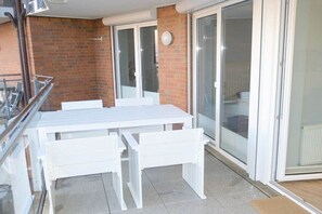 A balcony with a white table and benches, a glass door leading to a room, and a brick wall. - Beach Palace Apt. 108 (Cuxhaven)
