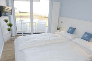 A bedroom with a bed, a TV, and a view of an outdoor area with tables. - Beach Palace Apt. 108 (Cuxhaven)