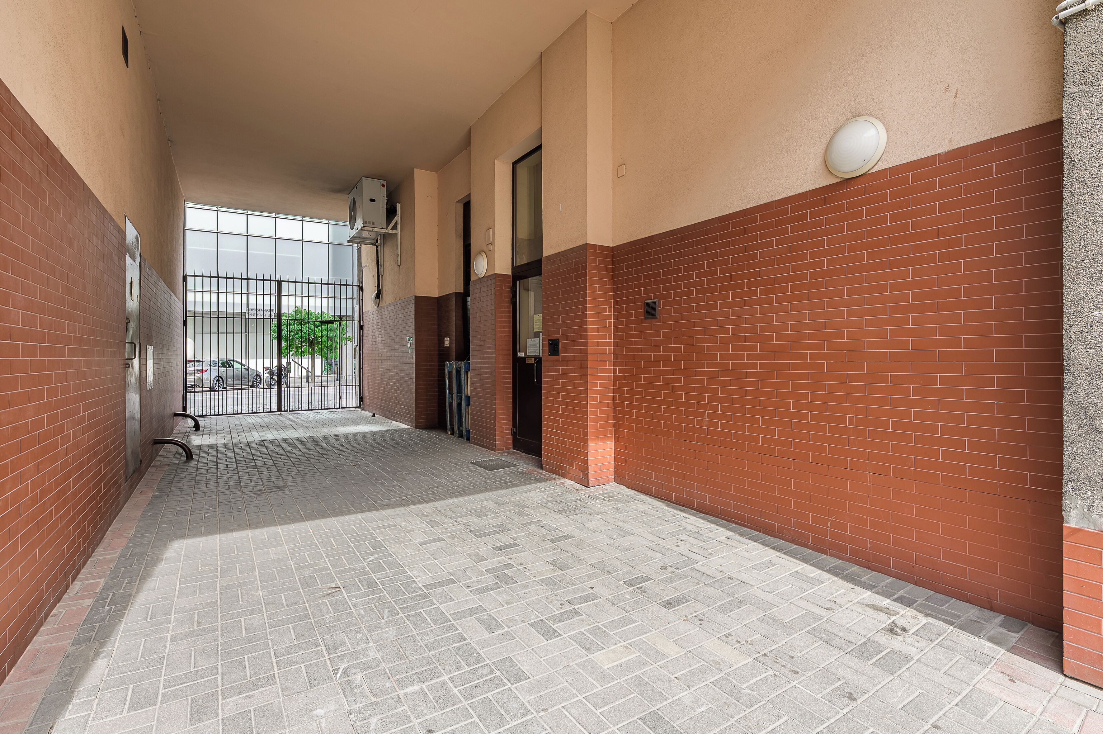 A corridor with a tiled floor, brick walls, and a glass door leading to an outdoor area.