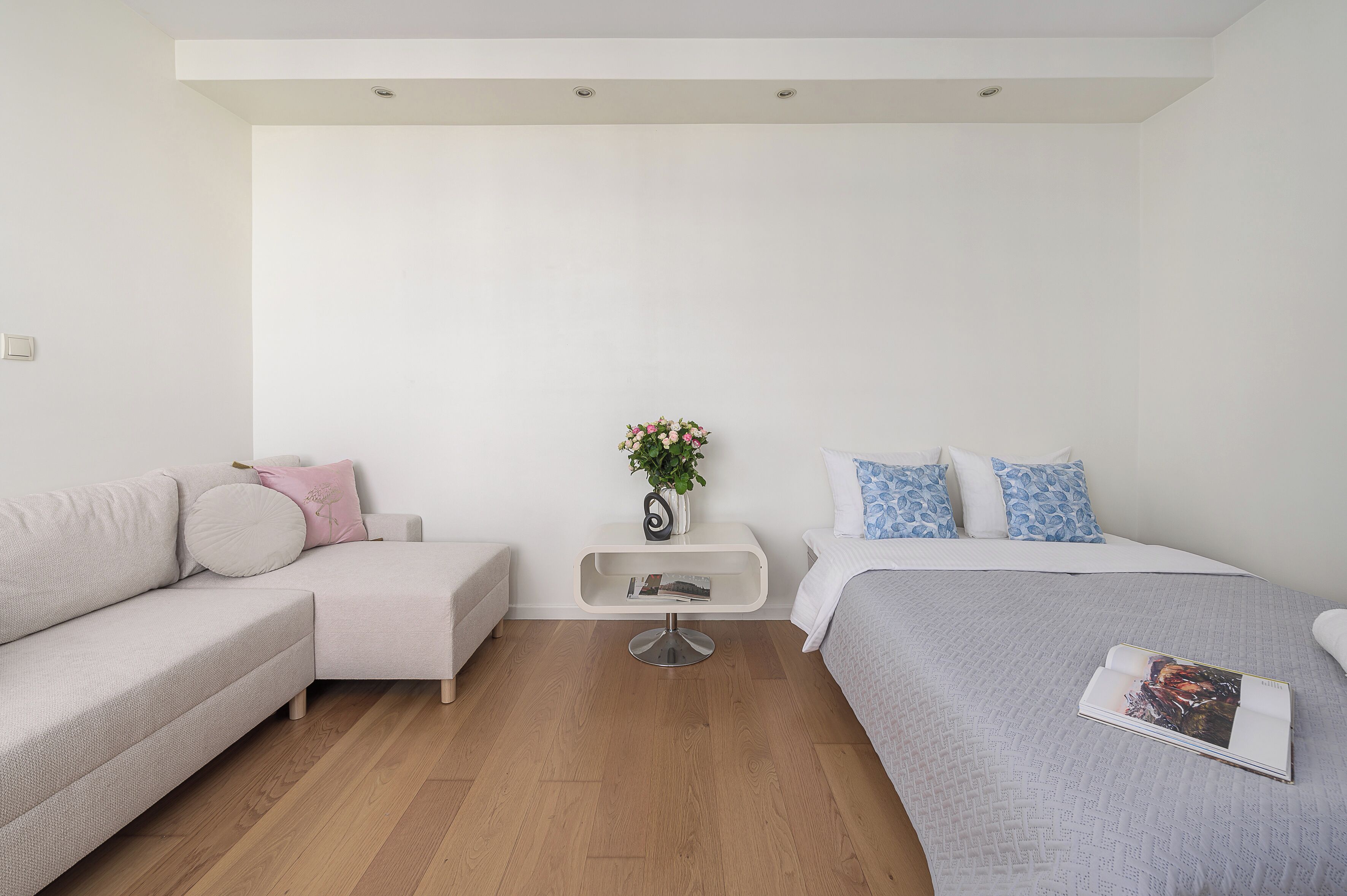Quarto moderno com sofá, mesinha lateral com um vaso e cama com almofadas estampadas.