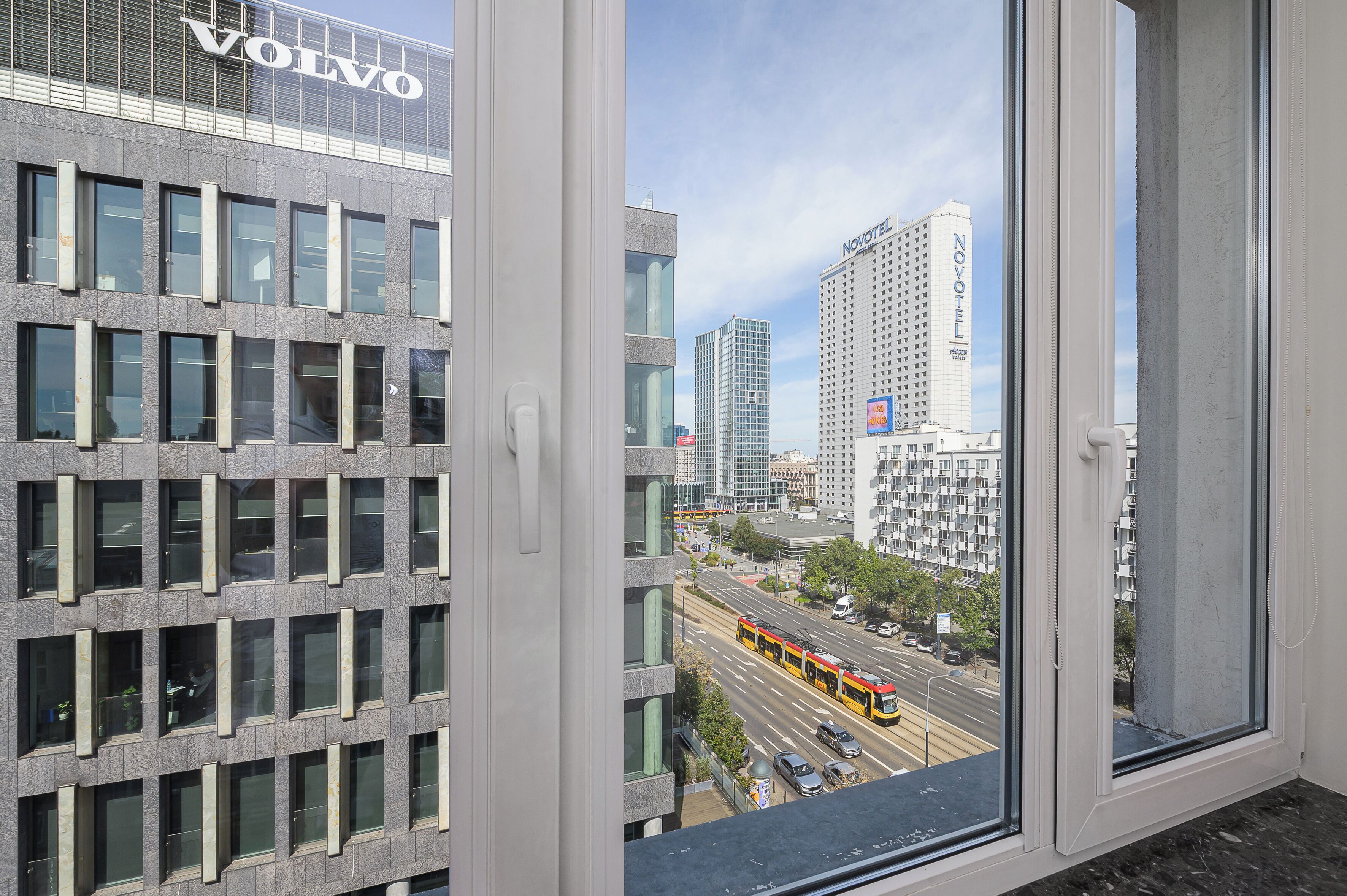 A cityscape with modern buildings, including a hotel named Novotel, and a tram in the foreground.