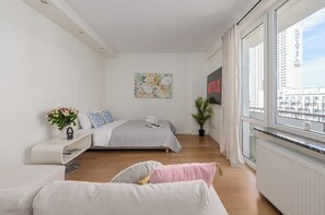 Een moderne slaapkamer met een bed, een bank, een raam met uitzicht op de stad en een aan de muur bevestigd kunstwerk.