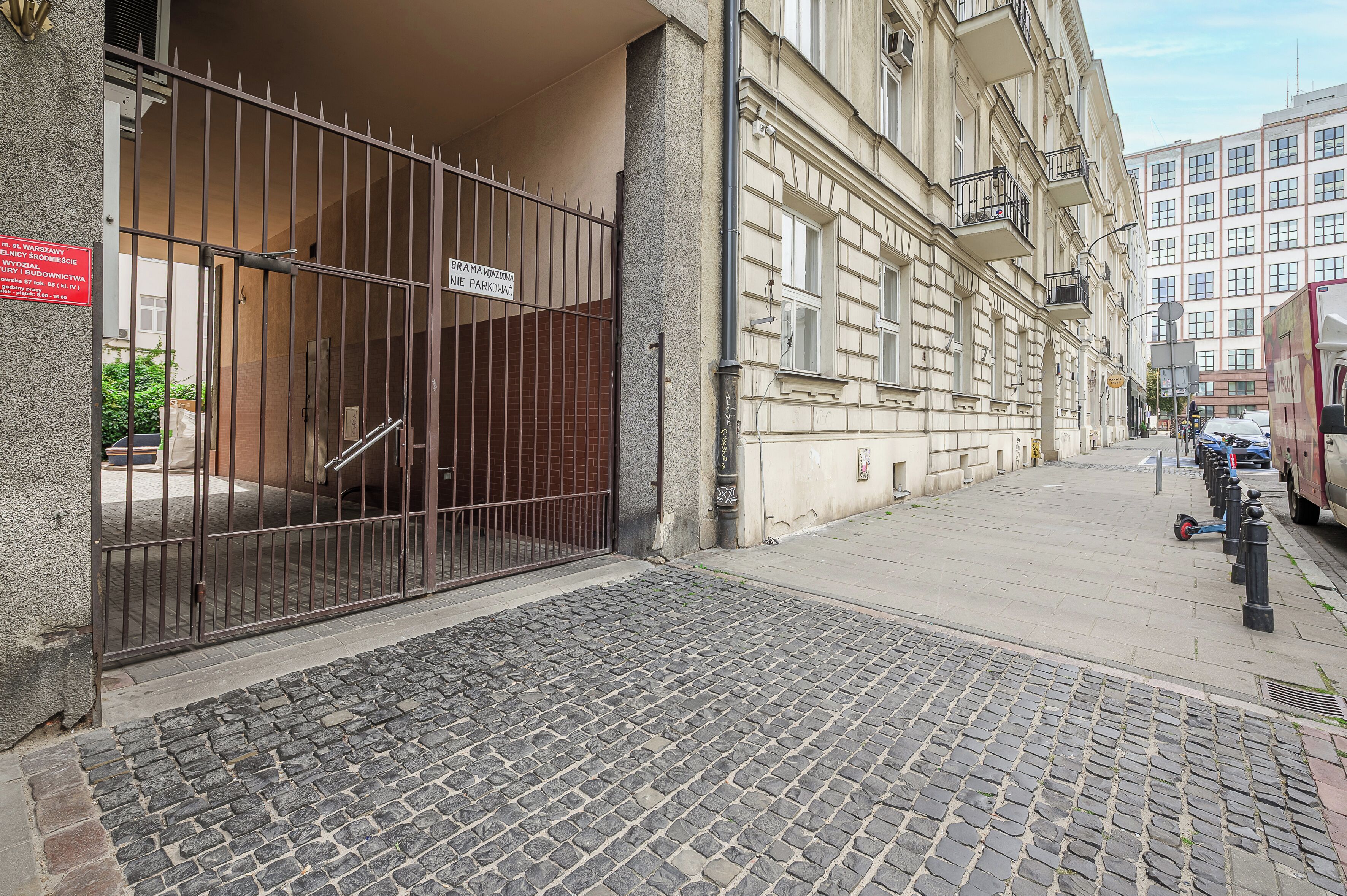 Entrada d'un edifici amb una reixa metàl·lica, un camí empedrat i un patinet aparcat.