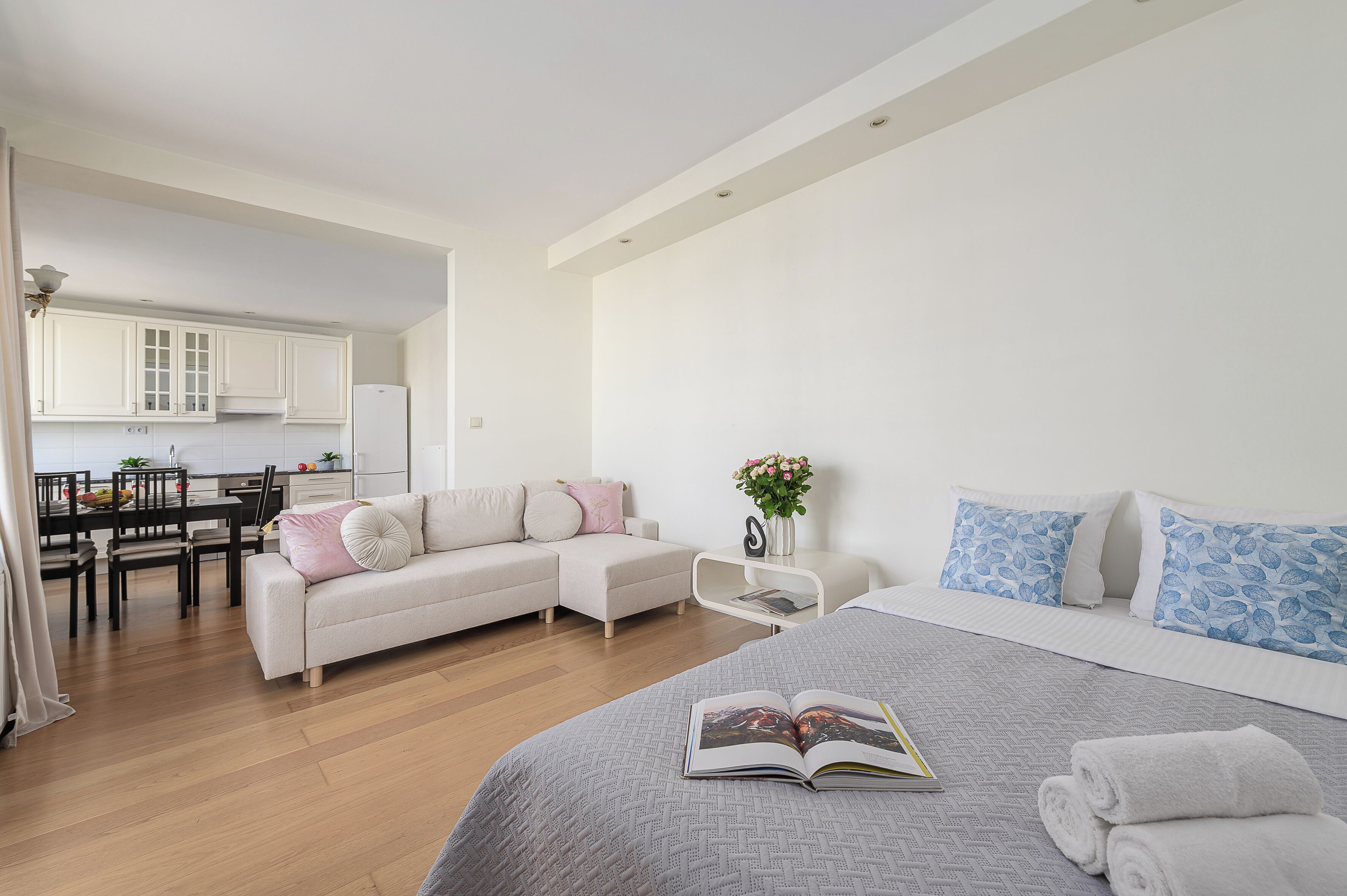 A modern bedroom with a large bed, a sofa, a dining area, and a kitchen.