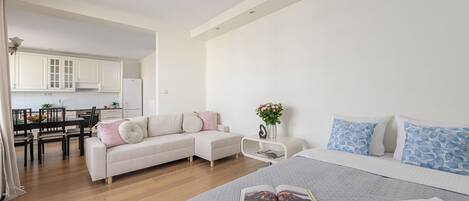 A modern bedroom with a large bed, a sofa, a dining area, and a kitchen.