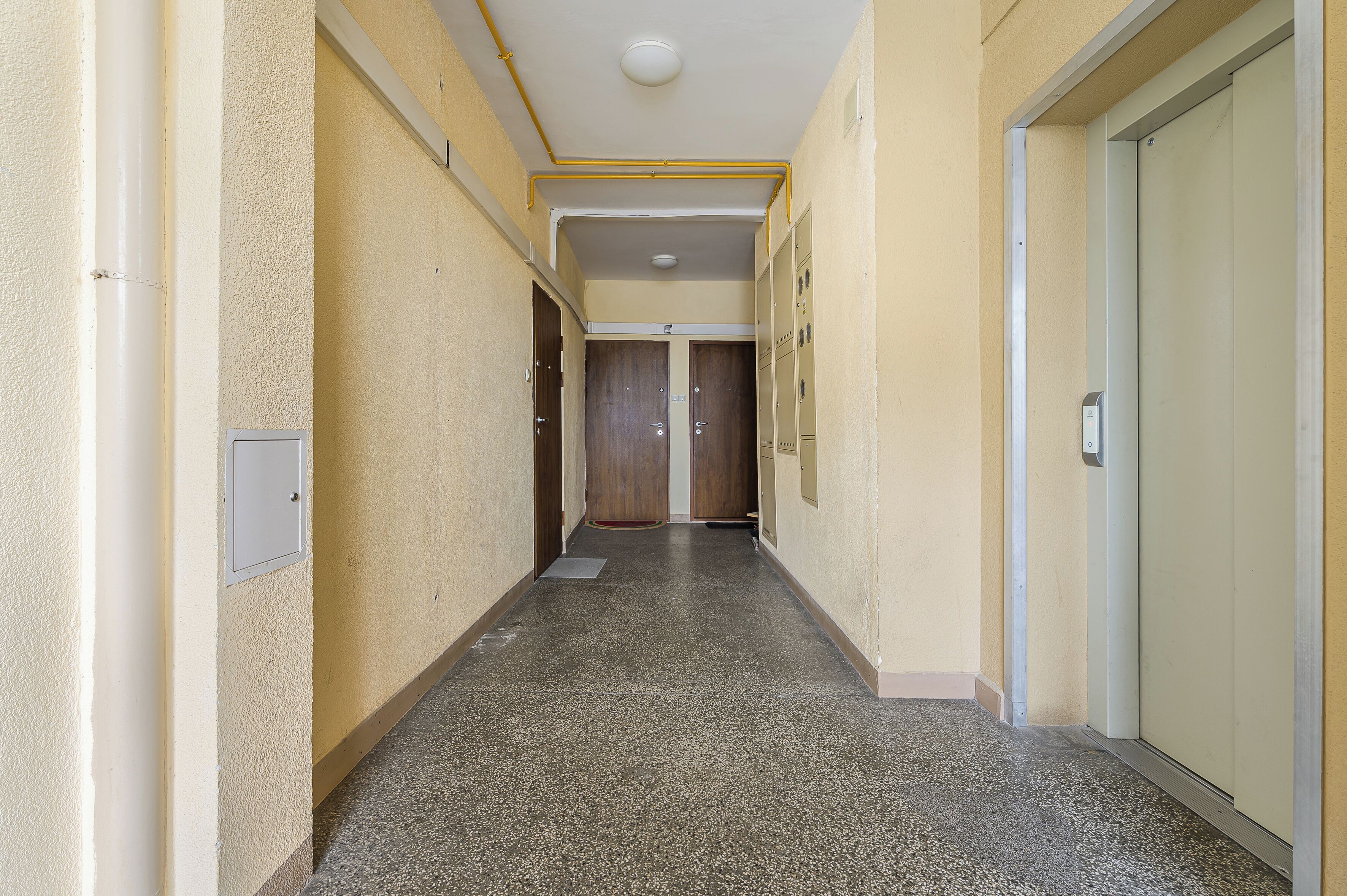 A hallway with lockers, a door at the end, and a light fixture on the ceiling.