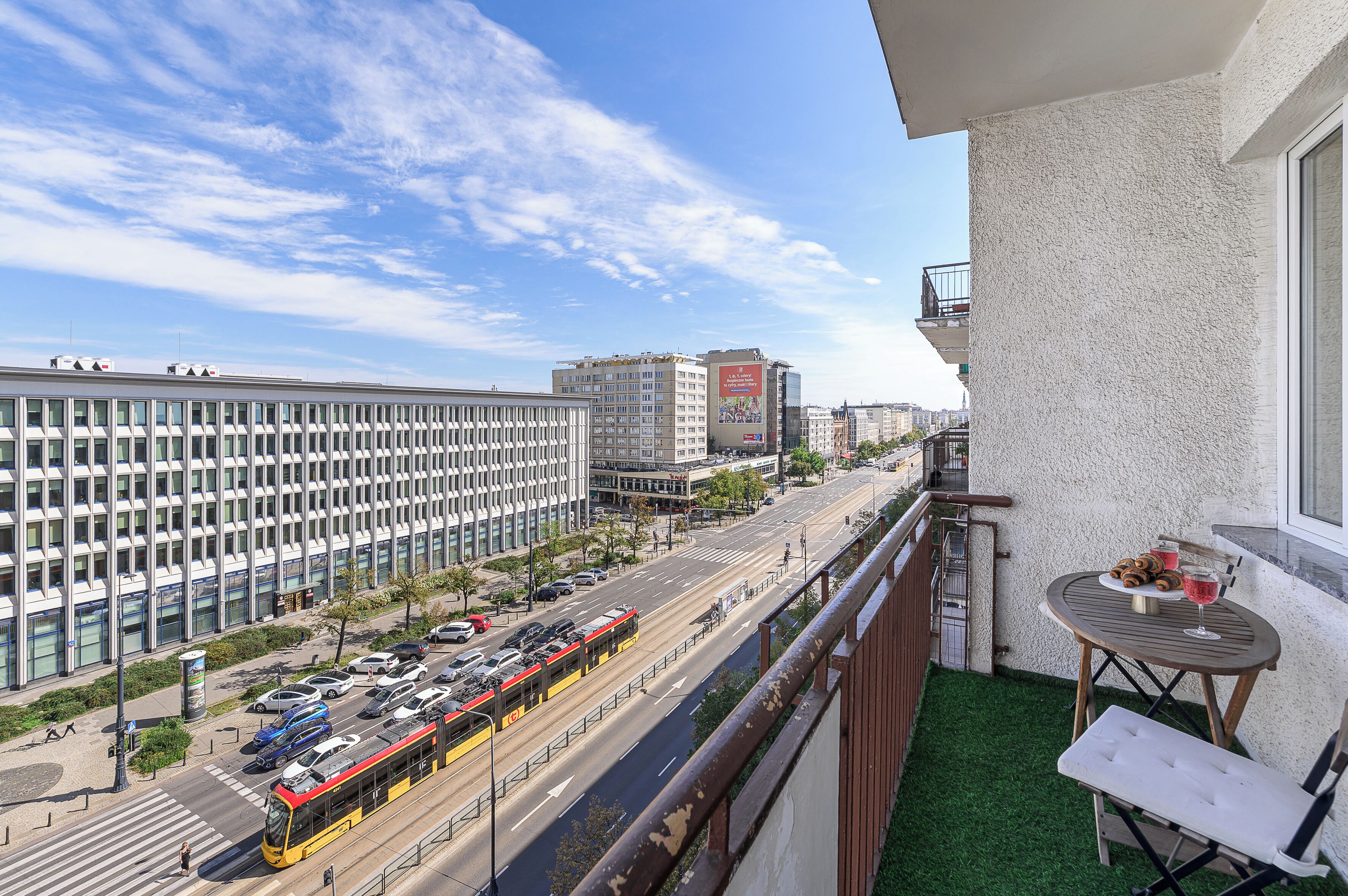 A balcony with a view of a city street, a tram, and a building with a large billboard.