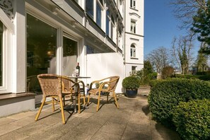 An outdoor seating area with wicker chairs and a table, a potted plant, and a hedge. - Beachcomber at Villa Stranddistel (Binz)