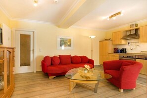 A living room with a red sofa, a glass coffee table, and a kitchen area with wooden cabinets. - Beachcomber at Villa Stranddistel (Binz)