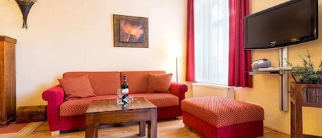 Una sala de estar con un sofá rojo, una mesa de centro de madera y un televisor de pantalla plana montado en la pared.