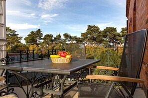 Eine Außenpatio mit einem Metalltisch und Stühlen, einer Obstkorb und Blick auf Bäume und einen Zaun.