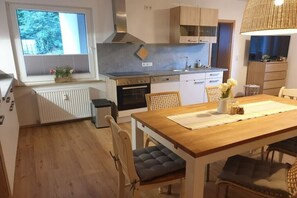 A modern kitchen with a built-in oven, a dining table with chairs, and a window with a view of trees. - Spring at Villa Waldrand (Bad Wünnenberg)