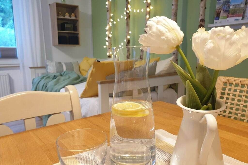 A dining table with a clear glass pitcher, a glass of water, and a white vase with white flowers.