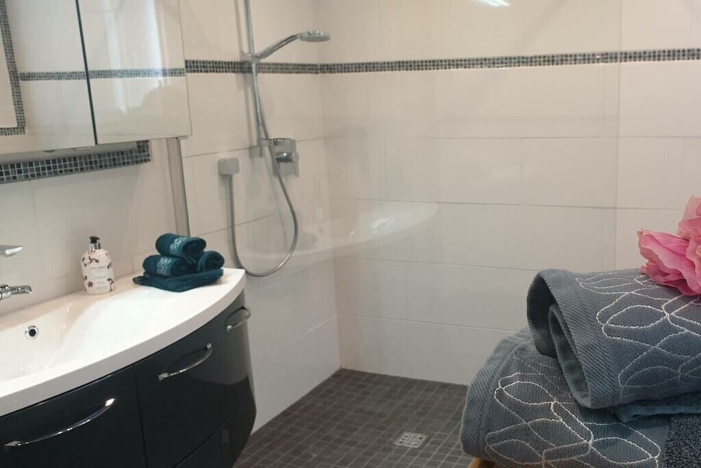 Een badkamer met een wit wastafel, donkere kastjes, een douche met een handdouche en een handdoek met een roze bloem.