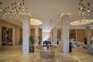 A spacious lobby with high ceilings, multiple chandeliers, a grand piano, and a variety of seating arrangements. - Lake Side Hotel (Qusar)