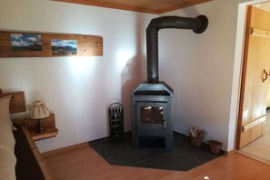 Ein Zimmer mit Kaminofen, einem Bett, einem Nachttisch, einer Lampe und einem Holzregal mit Bildern.
